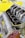 A close-up view of a high-performance engine, featuring multiple intake manifolds made of polished metal, partially unscrewed, revealing inner components. The engine has a sturdy, industrial design with a visible logo, set against a bright yellow background that highlights its mechanical complexity.
