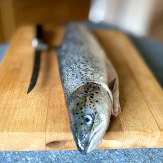 Fresh king fish fillets laid out neatly on a wooden board with herbs