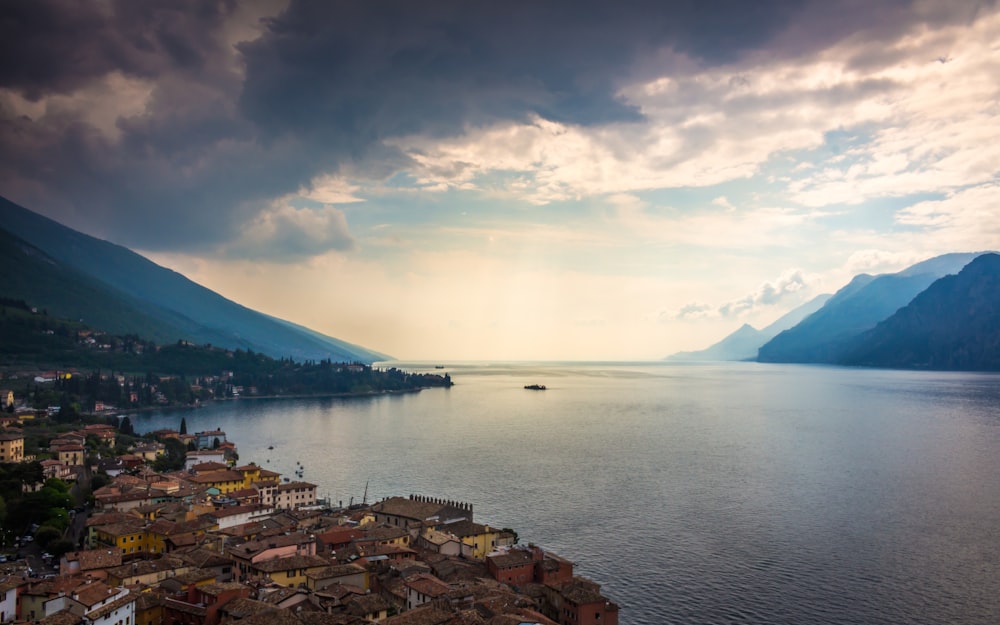 body of water near mountain under cloudy sky during daytime