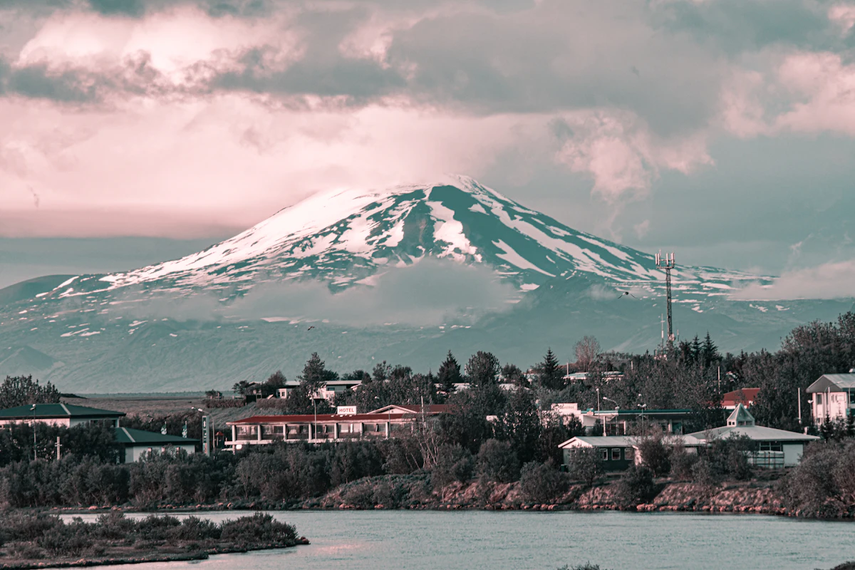 Houses and trees along a river in Hella, with a snow-covered mountain behind