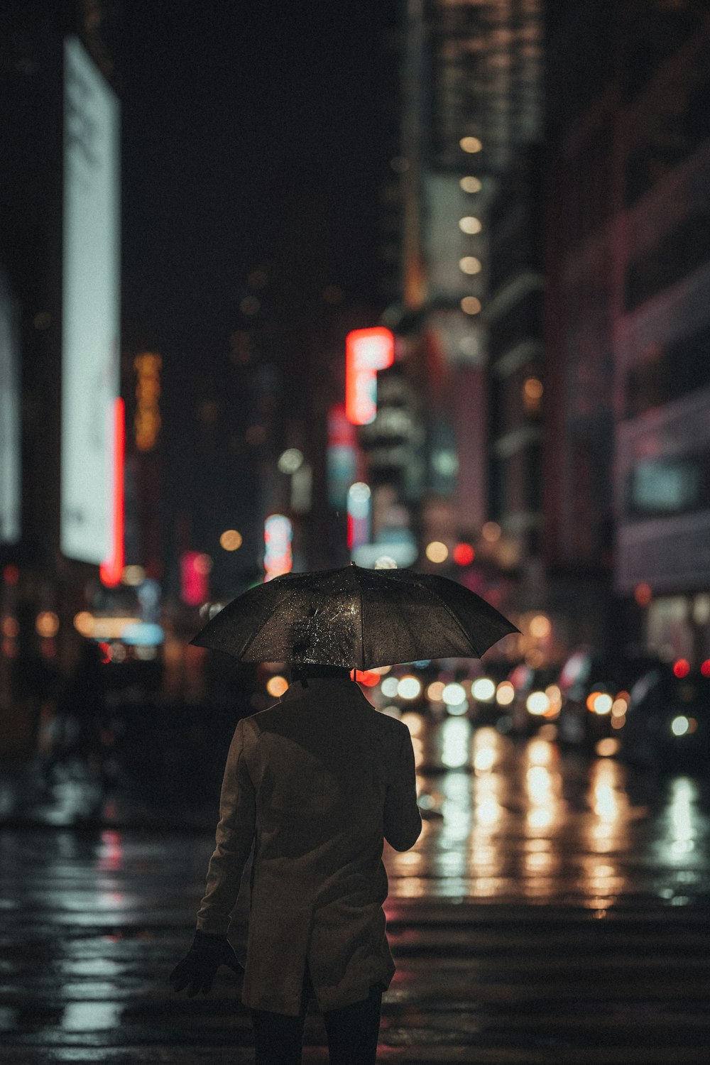 검은 코트를 입은 사람이 우산을 들고 밤 시간에 거리를 걷고 있다