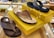 Three pairs of sandals are displayed on a glass surface with yellow boxes. The sandals have different brown and black straps and soles. There are small decorative lights adorning the boxes. In the background, various other footwear is visible on shelves.