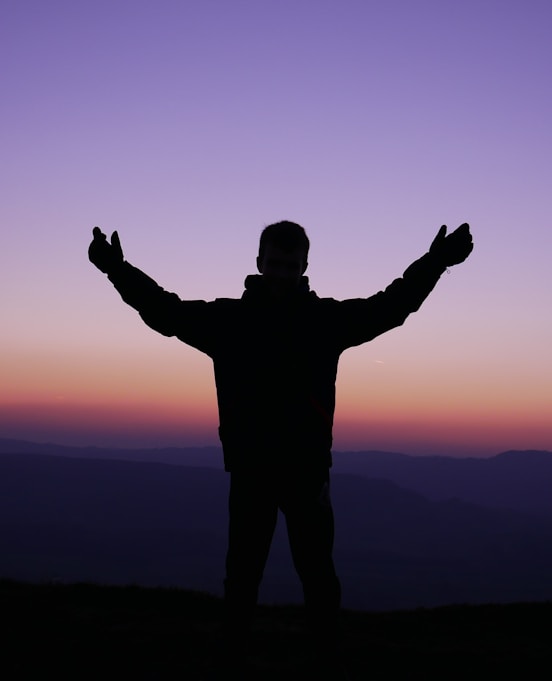 silhouette of man raising his hands during sunset