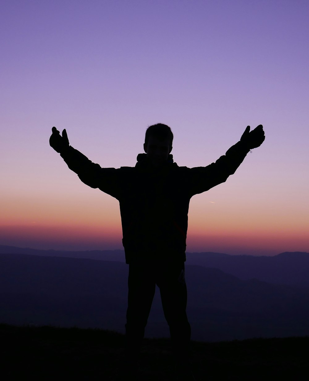 Silueta del hombre levantando las manos durante la puesta del sol