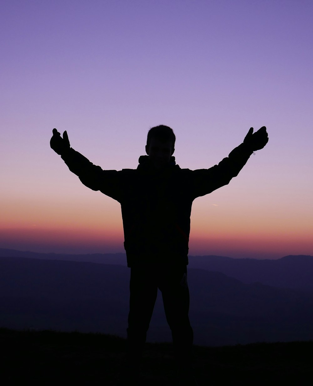 Silhouette de l’homme levant les mains au coucher du soleil