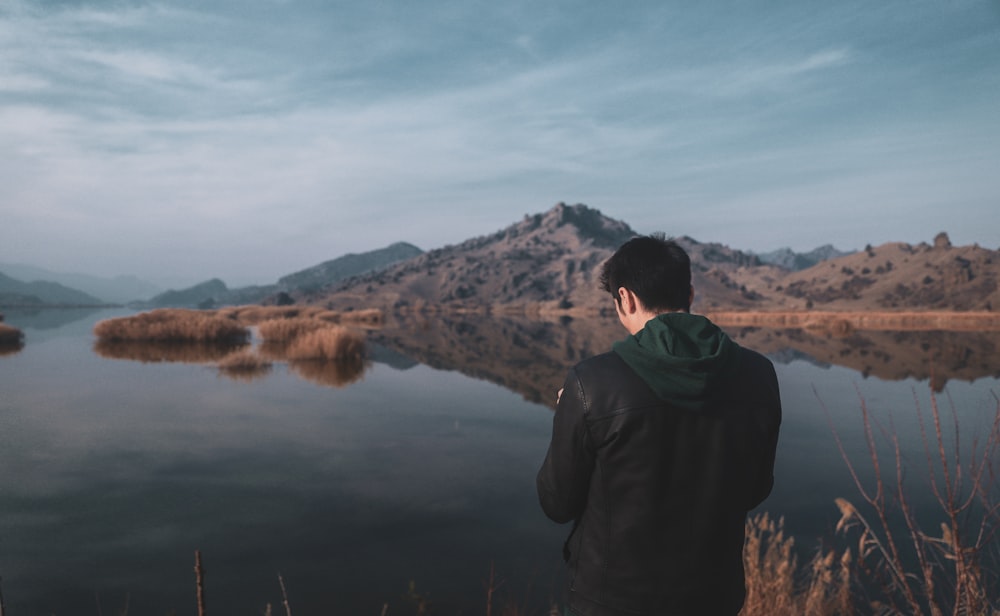 homme en veste noire debout près du lac pendant la journée