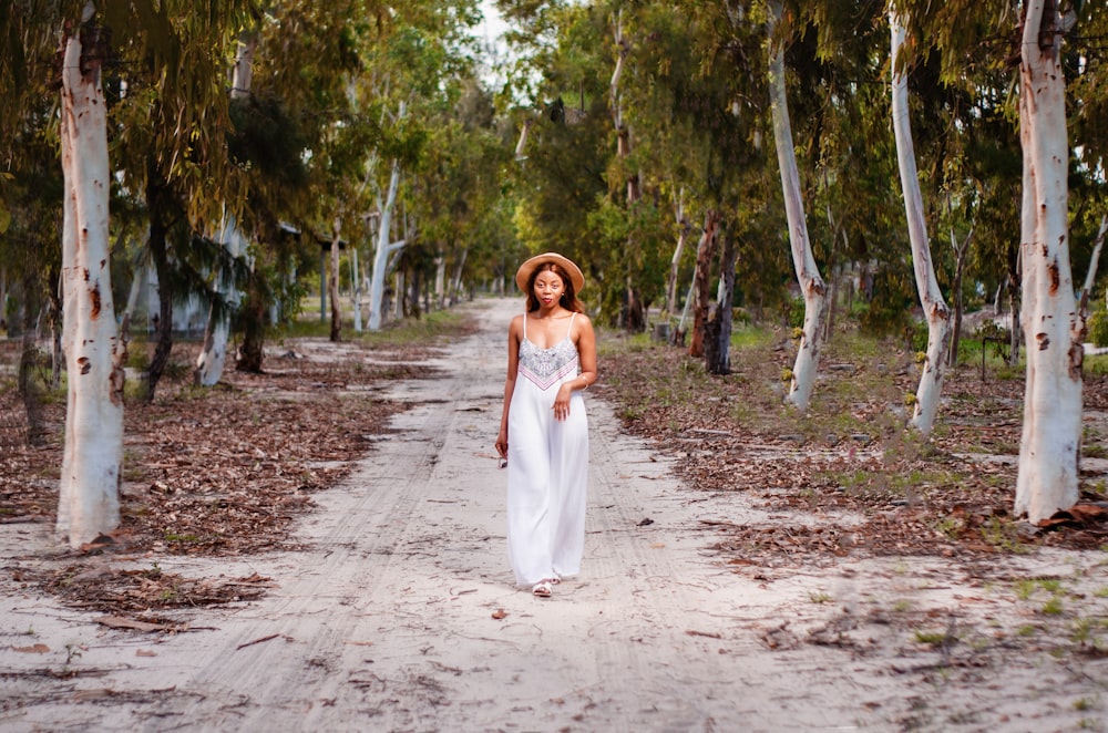 woman in white dress walking on dirt road between trees during daytime