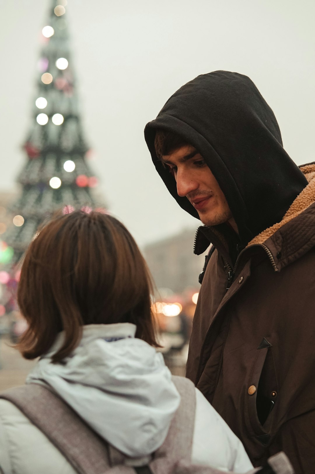man in brown hoodie standing beside woman in white coat