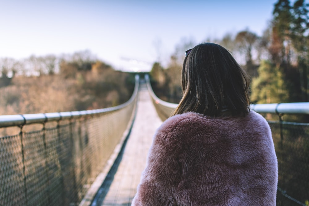 woman in brown fur coat standing on bridge during daytime