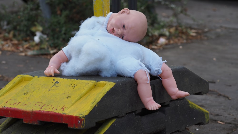 Baby in weißem Onesie liegt auf gelb-schwarzer Holzbank