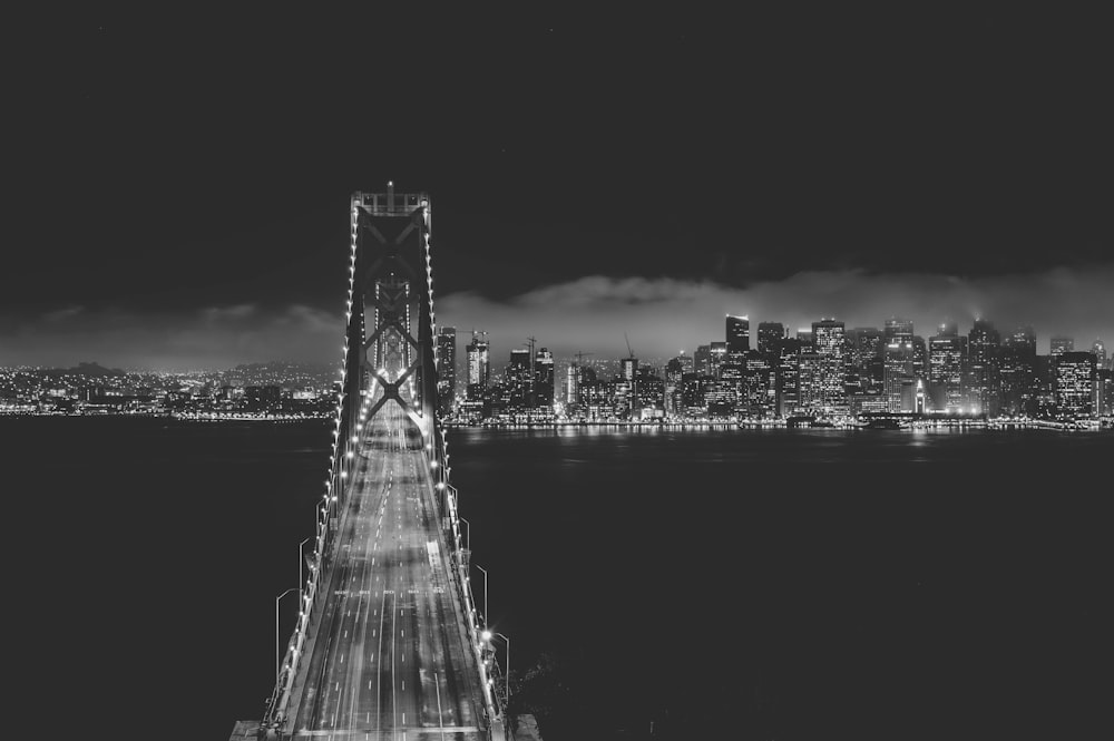 grayscale photo of bridge near city buildings