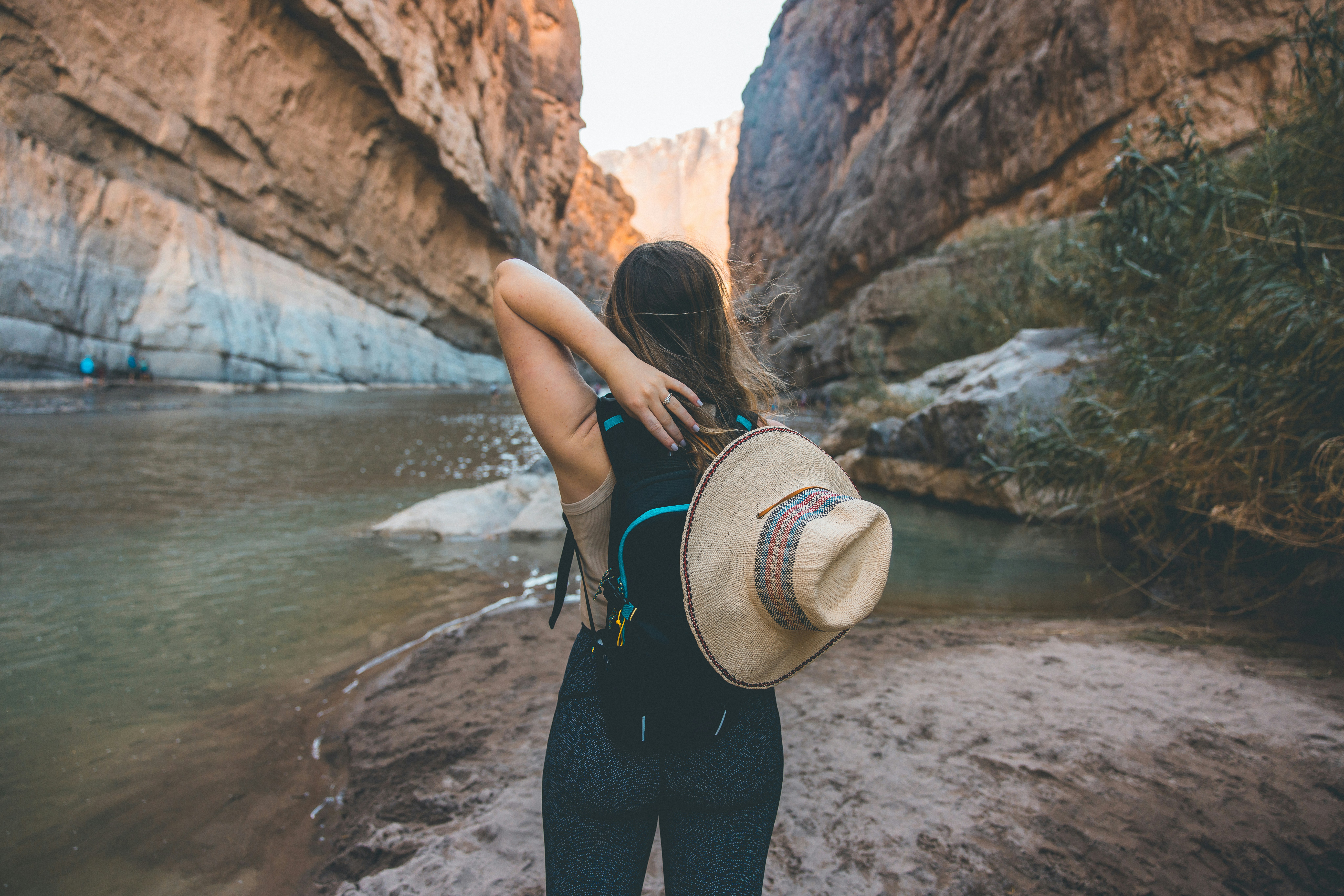woman in black tank top and black pants with brown hat standing on rocky shore during