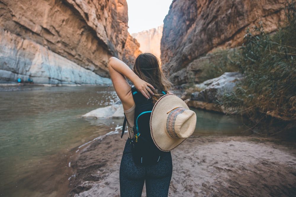 woman in black tank top and black pants with brown hat standing on rocky shore during