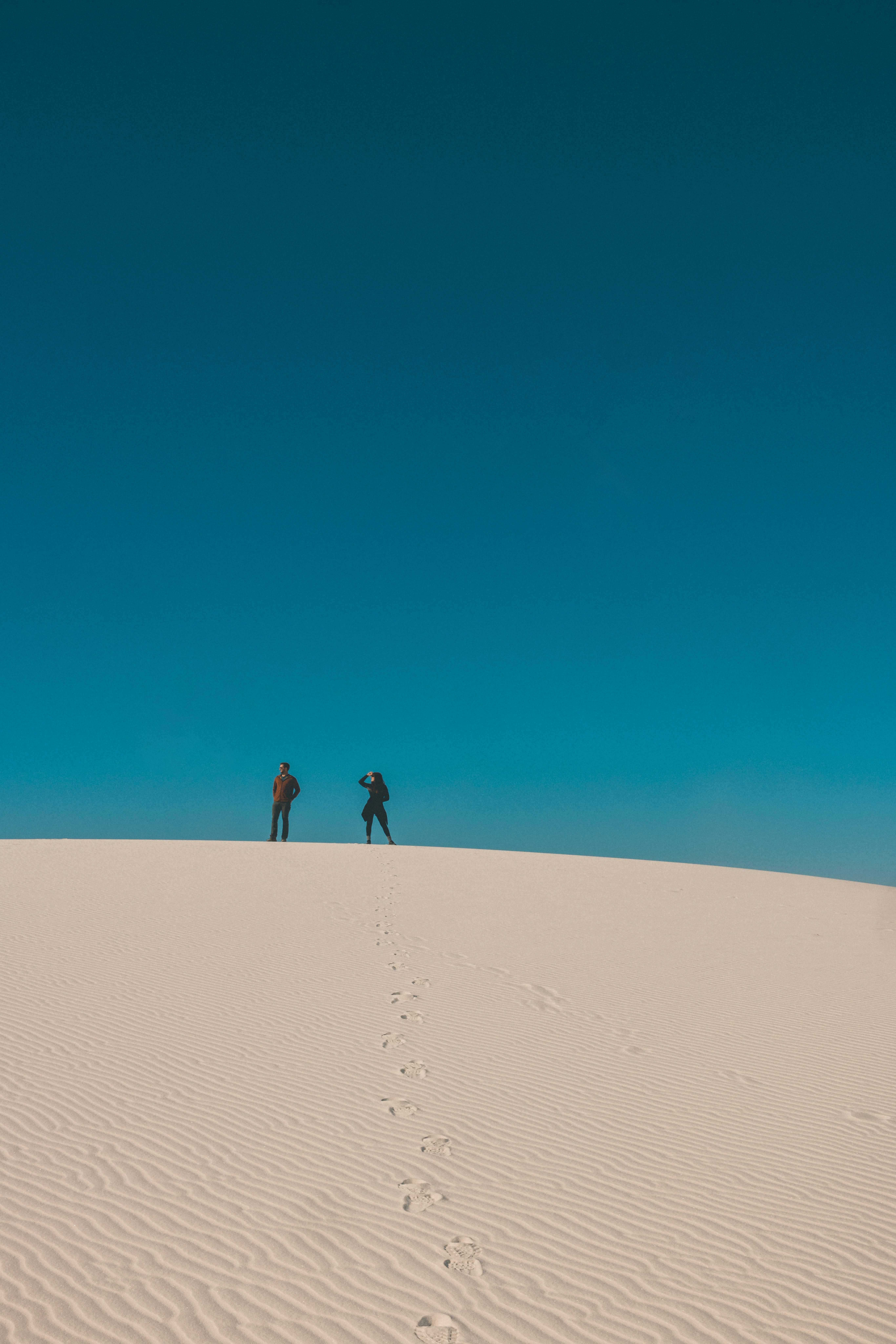 2 person walking on sand dunes during daytime