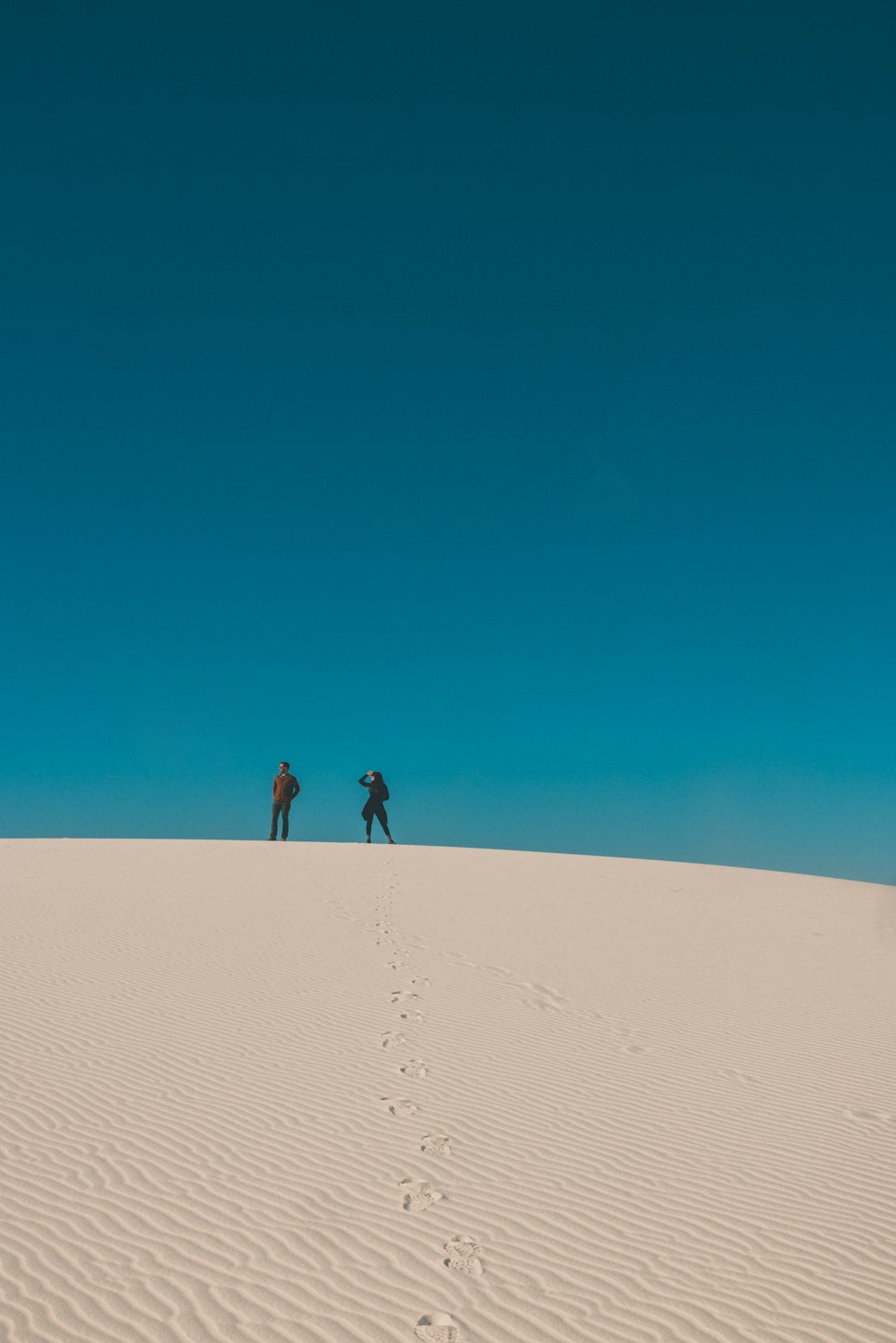 2 person walking on sand dunes during daytime