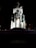 A monument featuring several sculpted busts arranged on cylindrical columns, illuminated dramatically against a dark background. The name 'Avram Iancu' is inscribed on the central structure. The lighting emphasizes the textures and details of the stone busts.