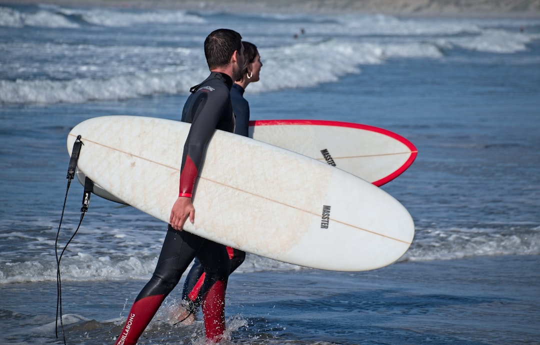 man in black wet suit holding white surfboard on water during daytime