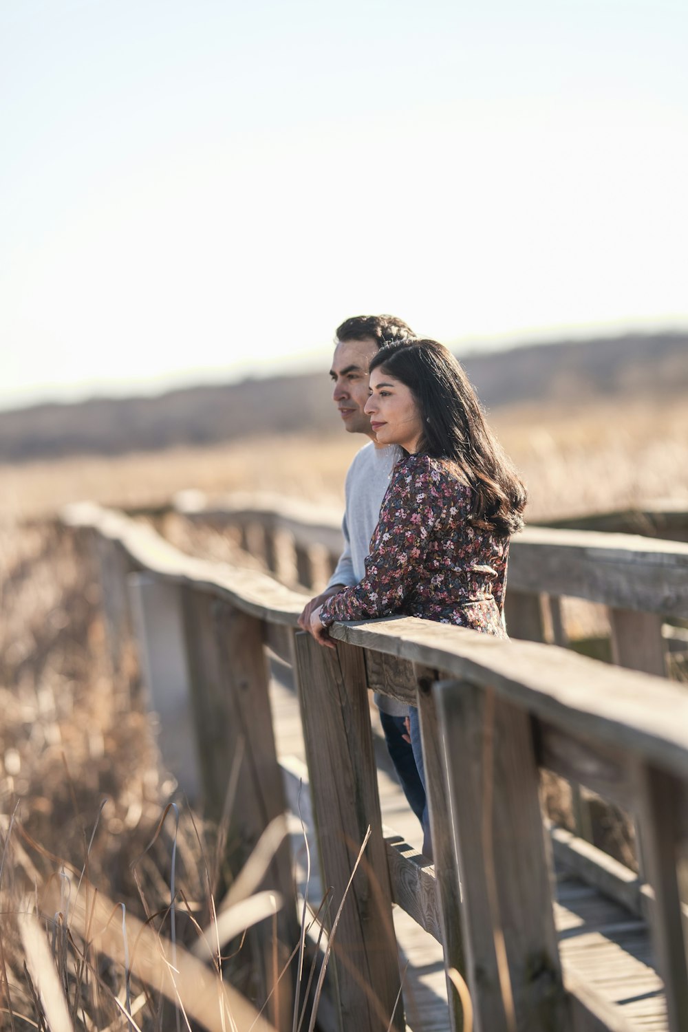 woman in white long sleeve shirt sitting on brown wooden fence during daytime