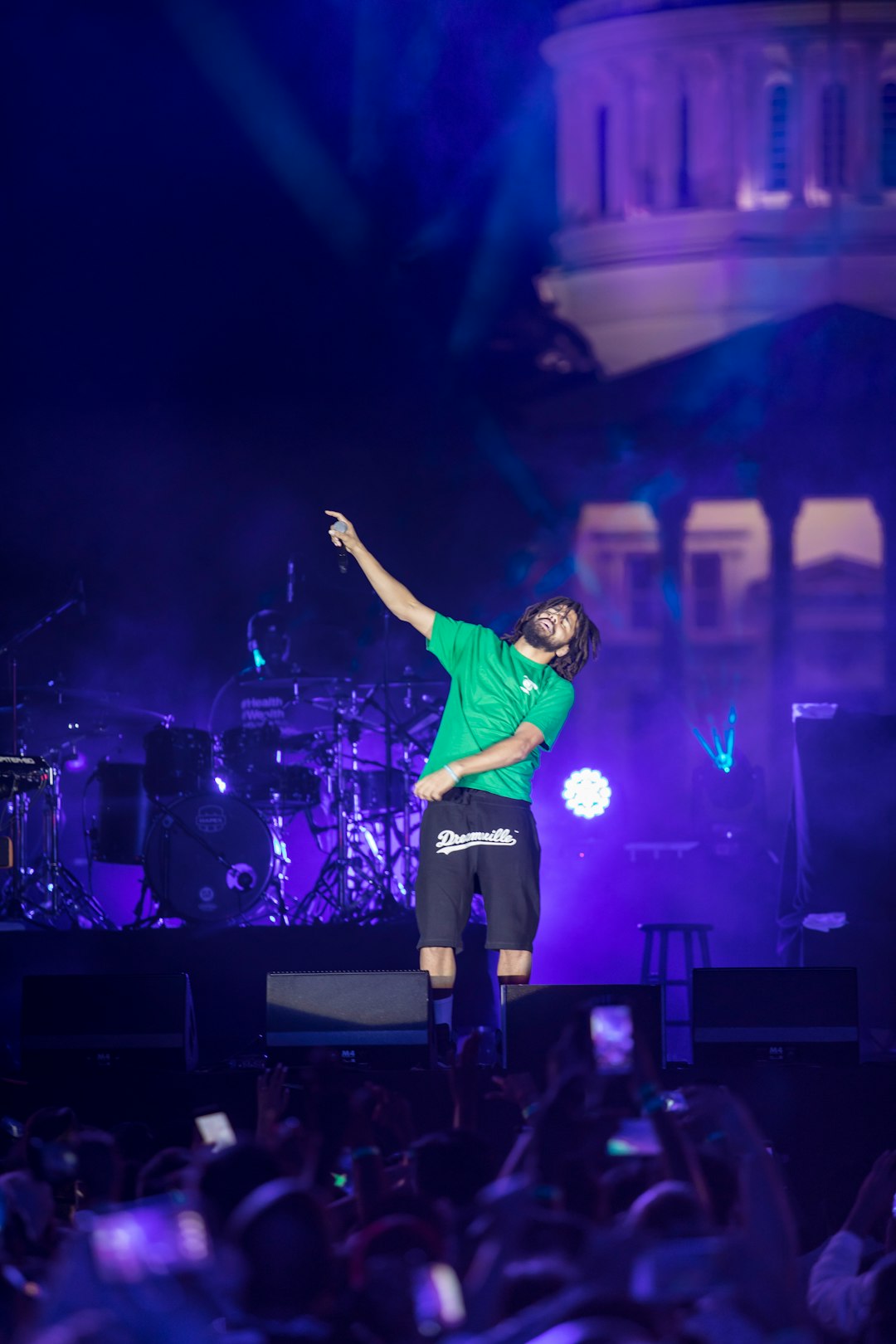 man in green shirt and black pants singing on stage