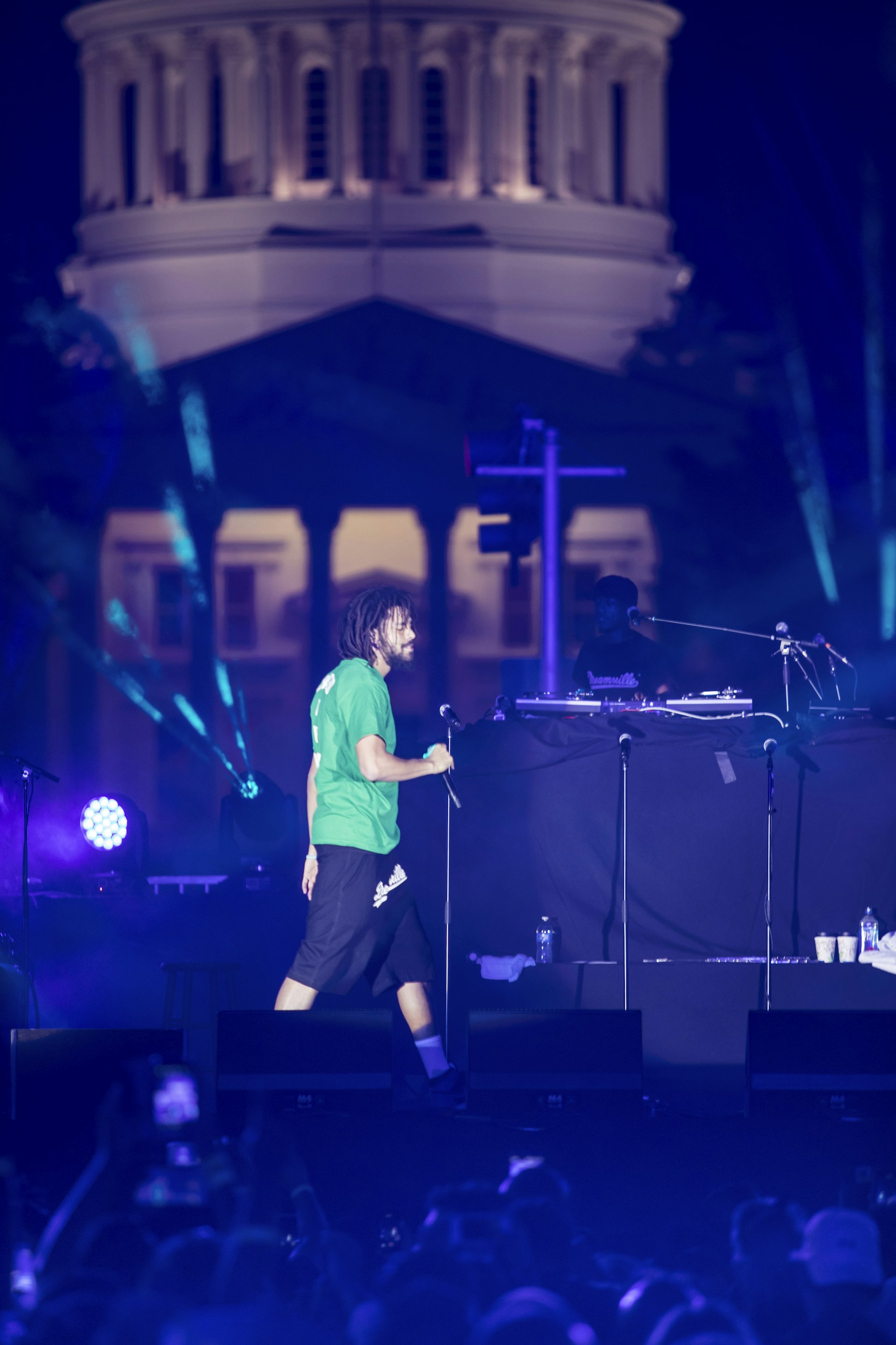 A dynamic shot of aneeq malik performing on stage, microphone in hand, with vibrant city lights glowing behind him.
