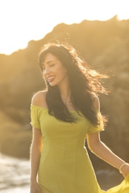 A woman in a soft sand-colored dress smiling outdoors with natural sunlight.
