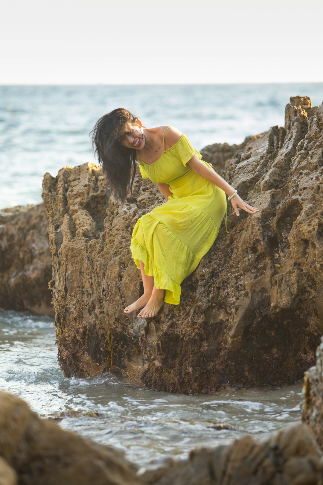 woman in yellow dress standing on rock near body of water during daytime