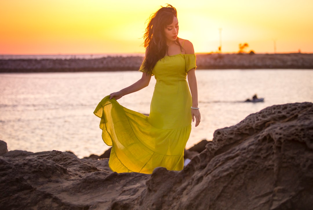 woman in yellow spaghetti strap dress standing on rock near body of water during daytime