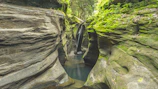 Beautiful hidden waterfall cascading over smooth rocks beside a narrow gorge in Ubud’s jungle
