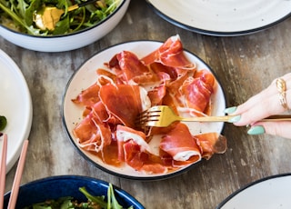 person holding chopsticks slicing meat on white ceramic plate