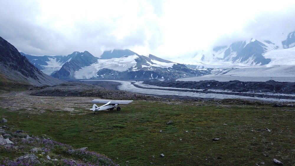 white airplane on green grass field near snow covered mountain during daytime