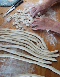 Close-up of hands rolling fresh pasta dough on a wooden table.