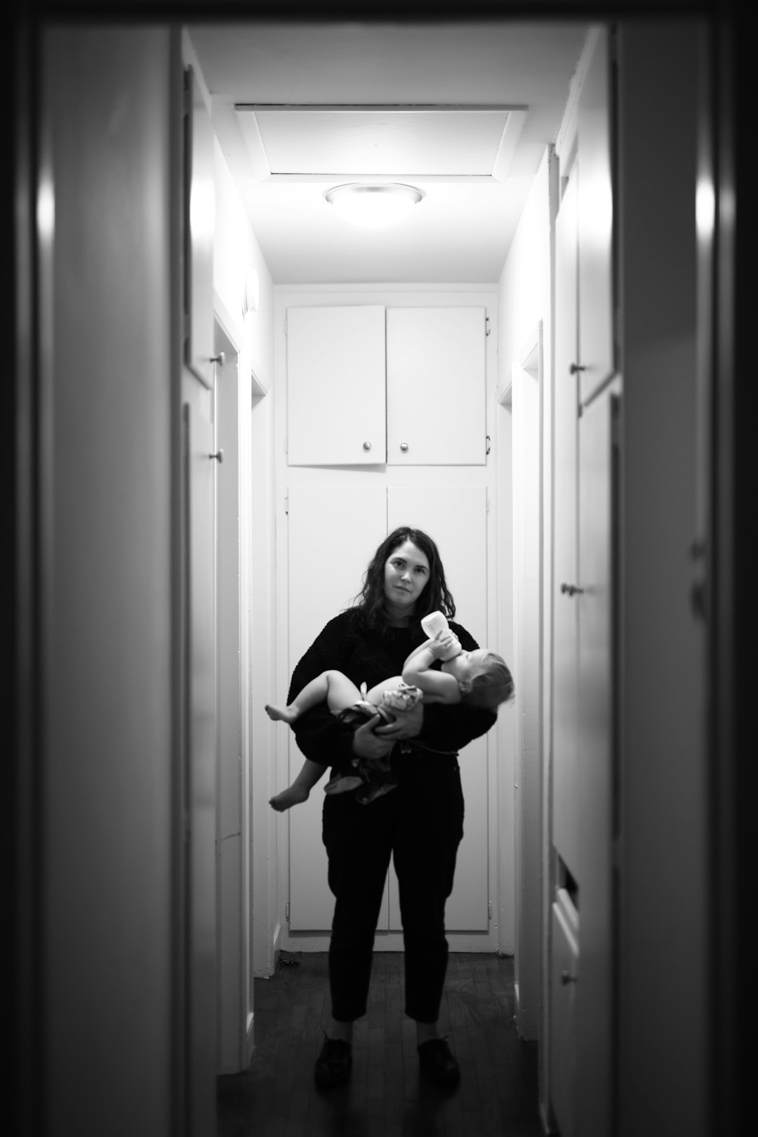 woman in black pants carrying baby in grayscale photography