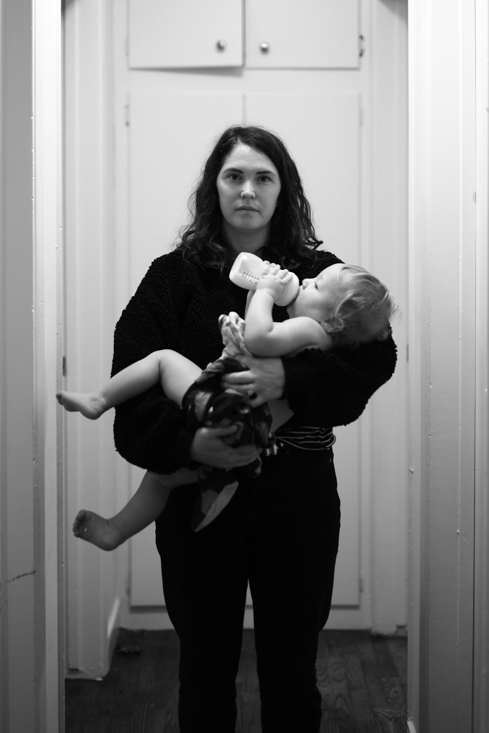 검은 긴 소매 셔츠를 입은 여자가 회색조 사진에서 아기를 안고 있다