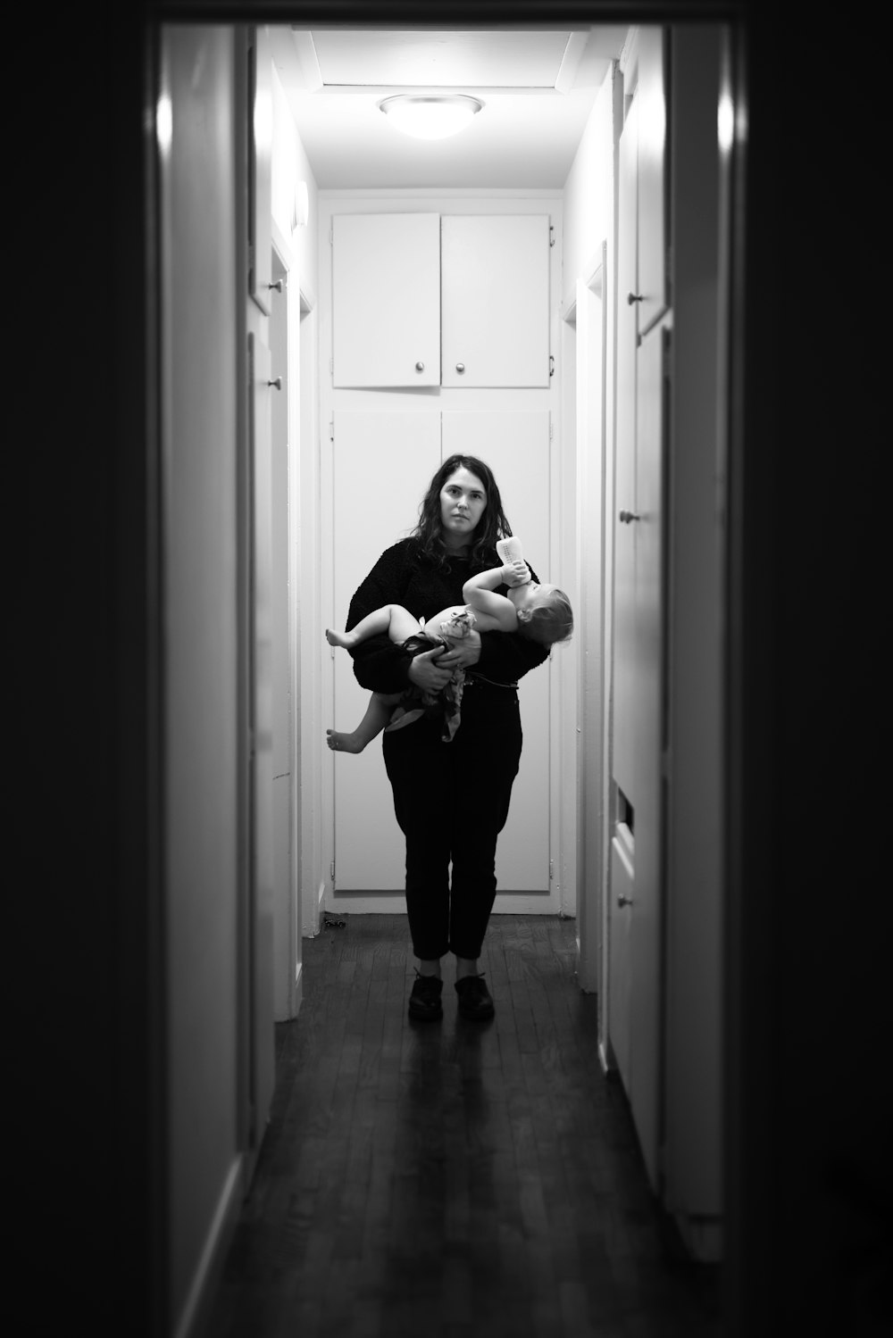mulher na camisa preta da manga comprida que transporta o bebê na fotografia em tons de cinza
