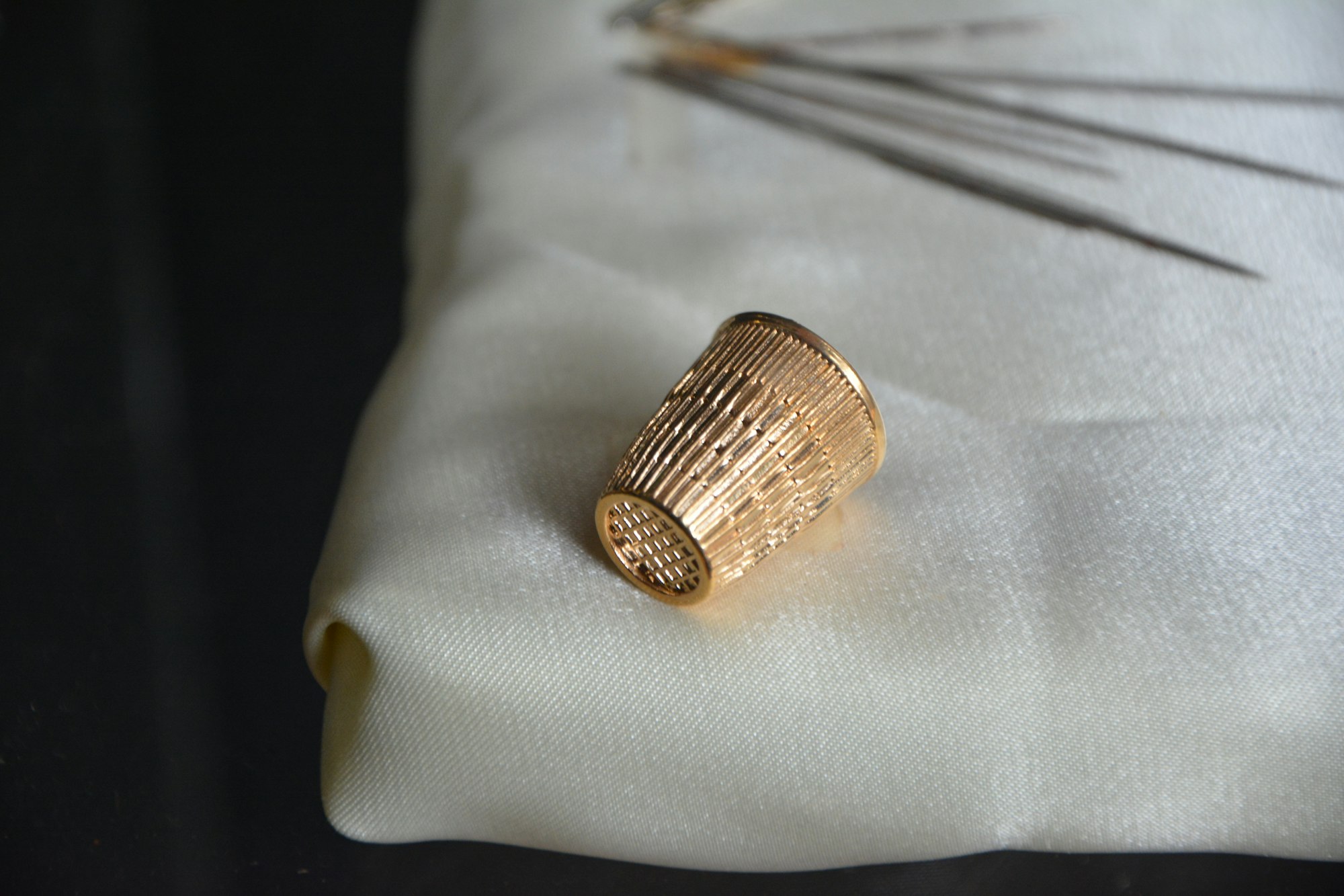 A golden metal thimble that is meant to be worn on the first joint of a finger.
