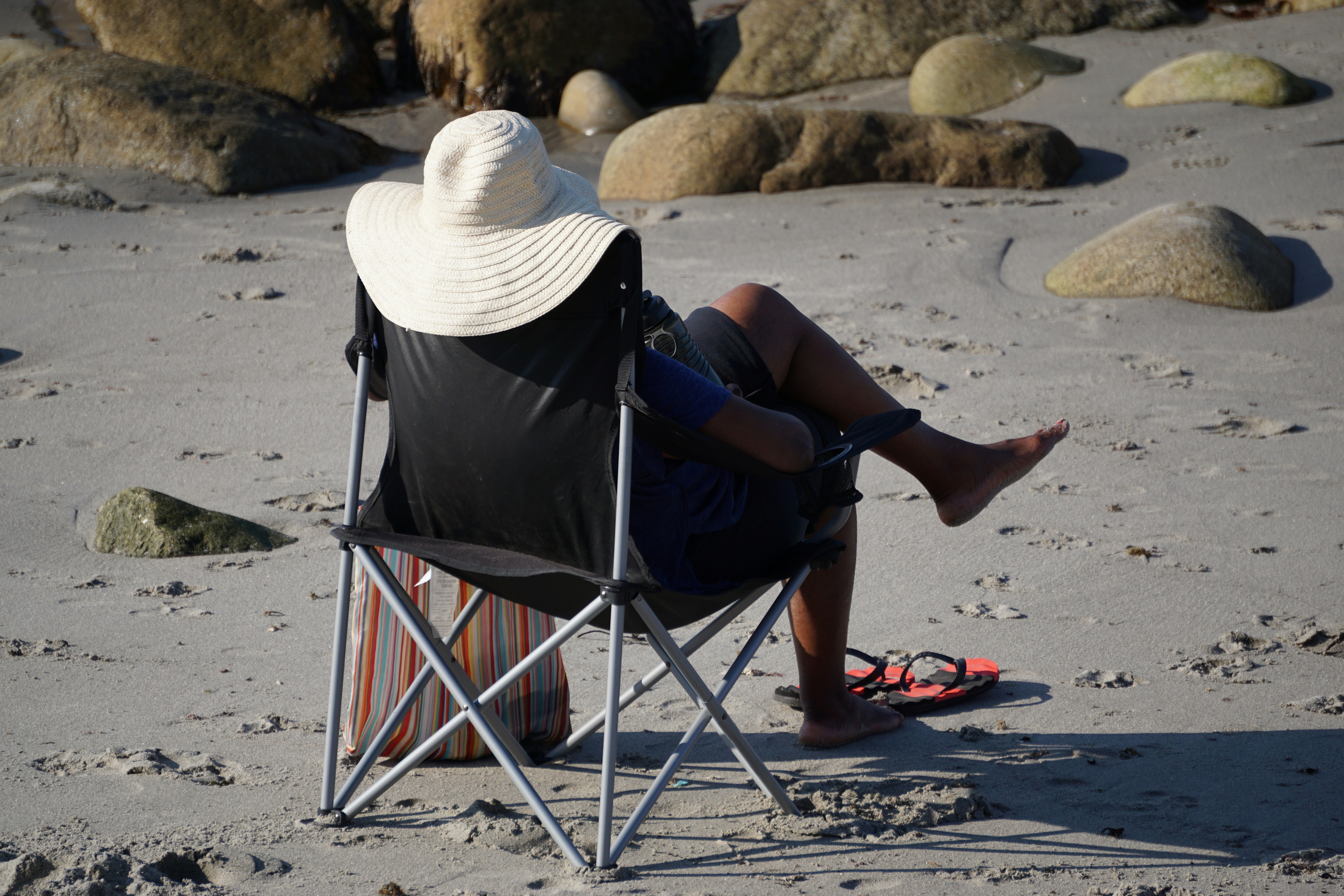 Woman hidden beneath a white straw hat on the beach.