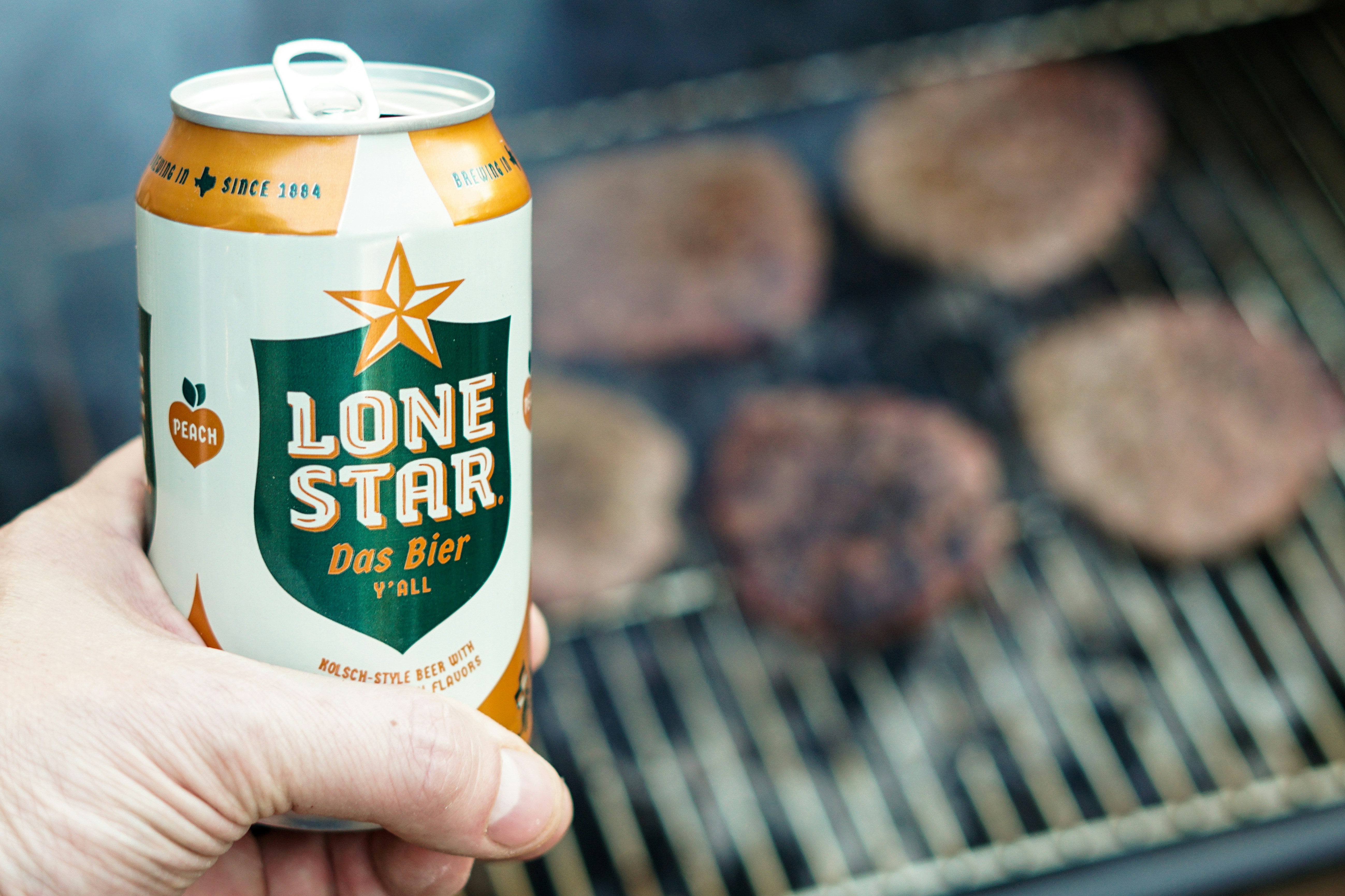Holding a ice cold Lone Star Beer from Texas outside while grilling hamburgers on a smokey outdoor charcoal grill.
