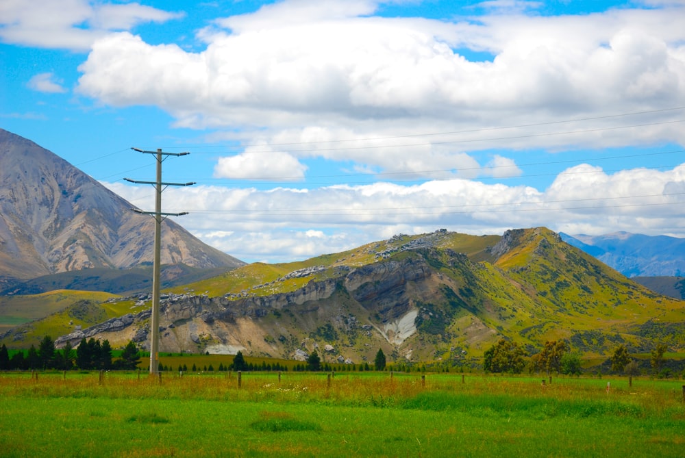 green grass field near mountain under white clouds during daytime