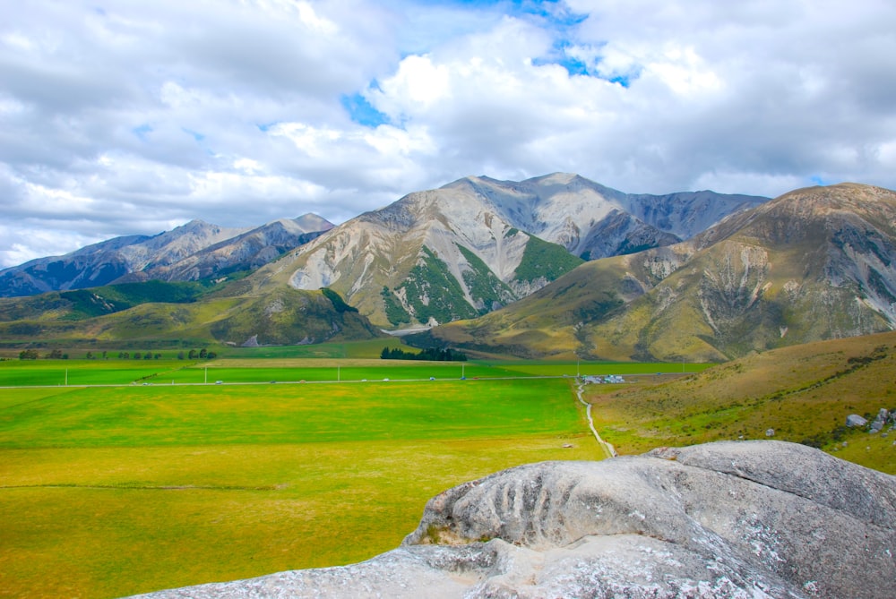 campo de grama verde perto da montanha sob nuvens brancas durante o dia