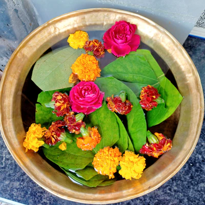 Close-up of a decorative brass urli with marigold flowers floating on water, set on a wooden table.
