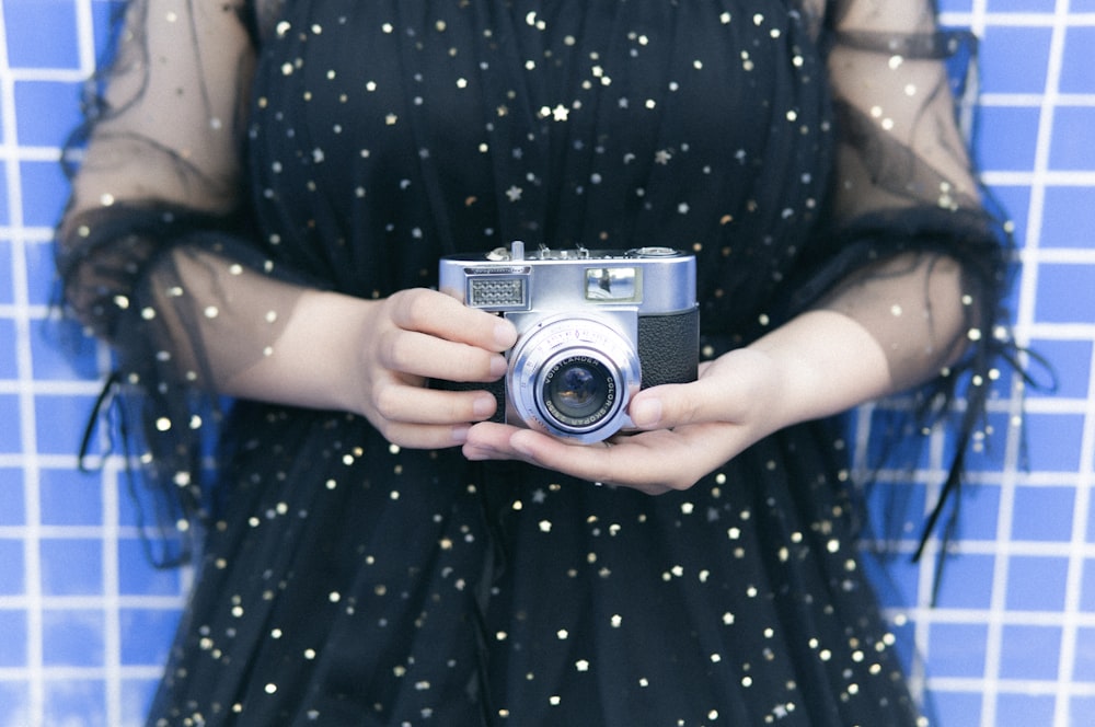 woman in blue and white polka dot dress holding silver and black camera