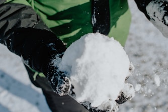 person in green and black jacket holding snow