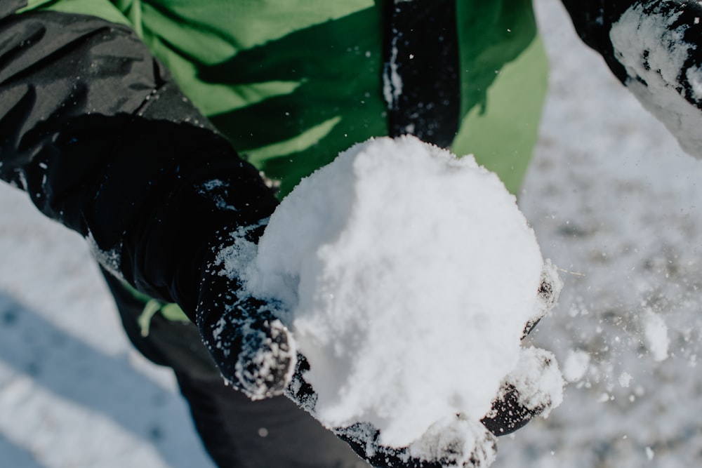 person in green and black jacket holding snow