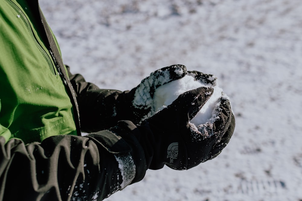 Person in grüner und schwarzer Jacke und schwarzer Hose, die tagsüber auf schneebedecktem Boden geht