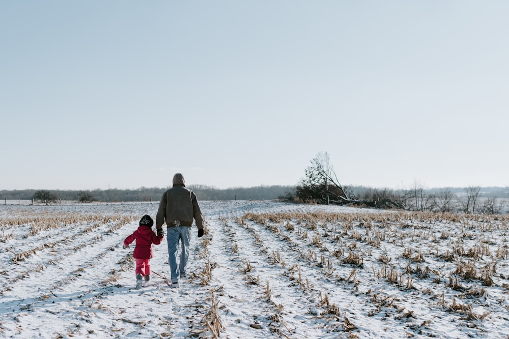 man and woman walking on snow covered field during daytime