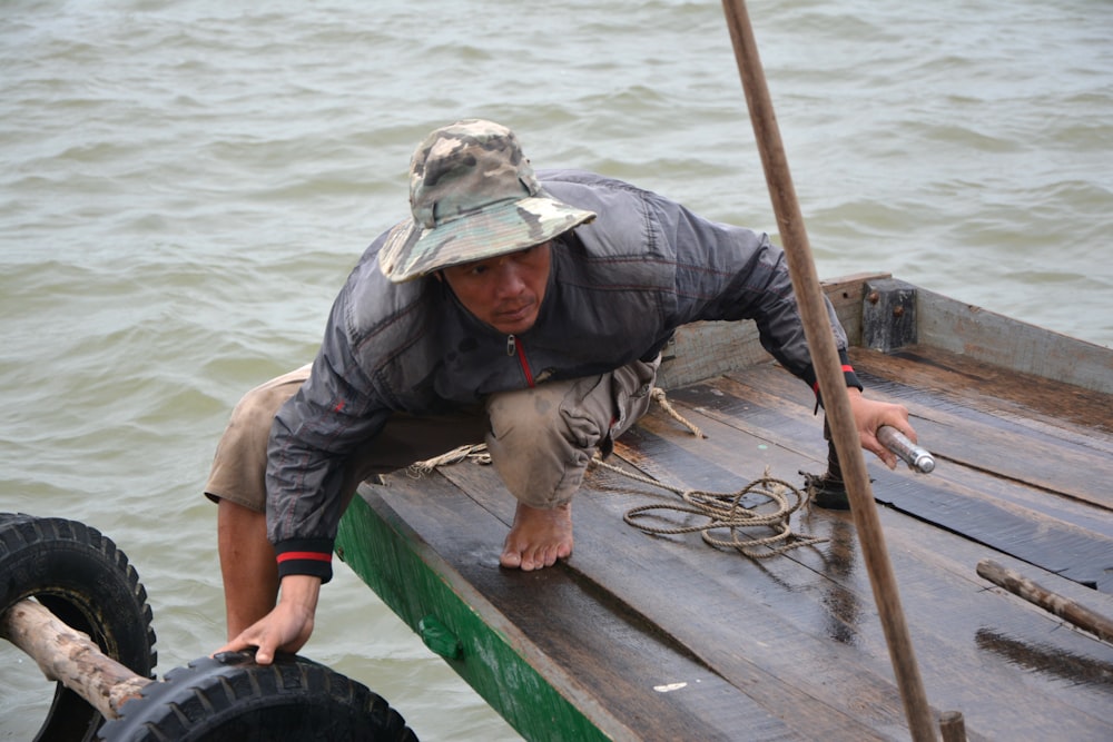 man in grey jacket and grey pants sitting on green wooden boat during daytime