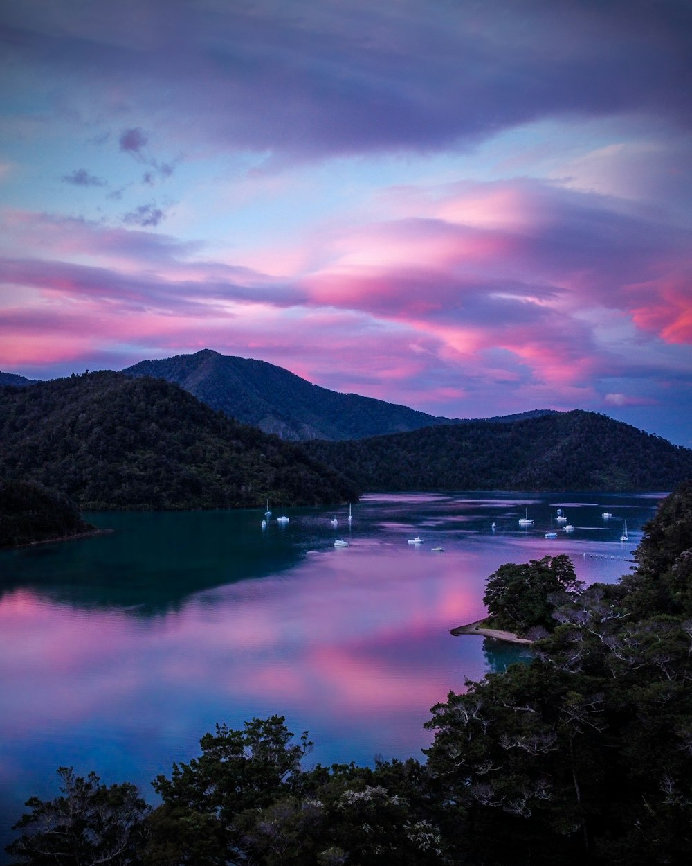 lake surrounded by trees and mountains under cloudy sky during daytime