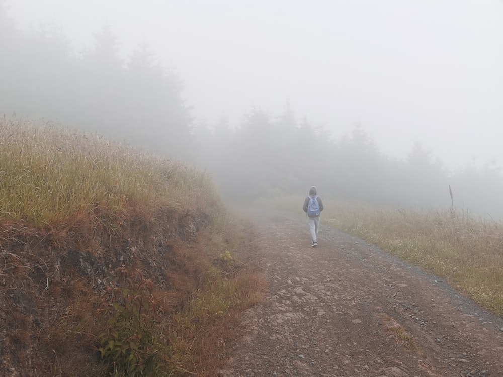 person in white jacket walking on dirt road during foggy weather