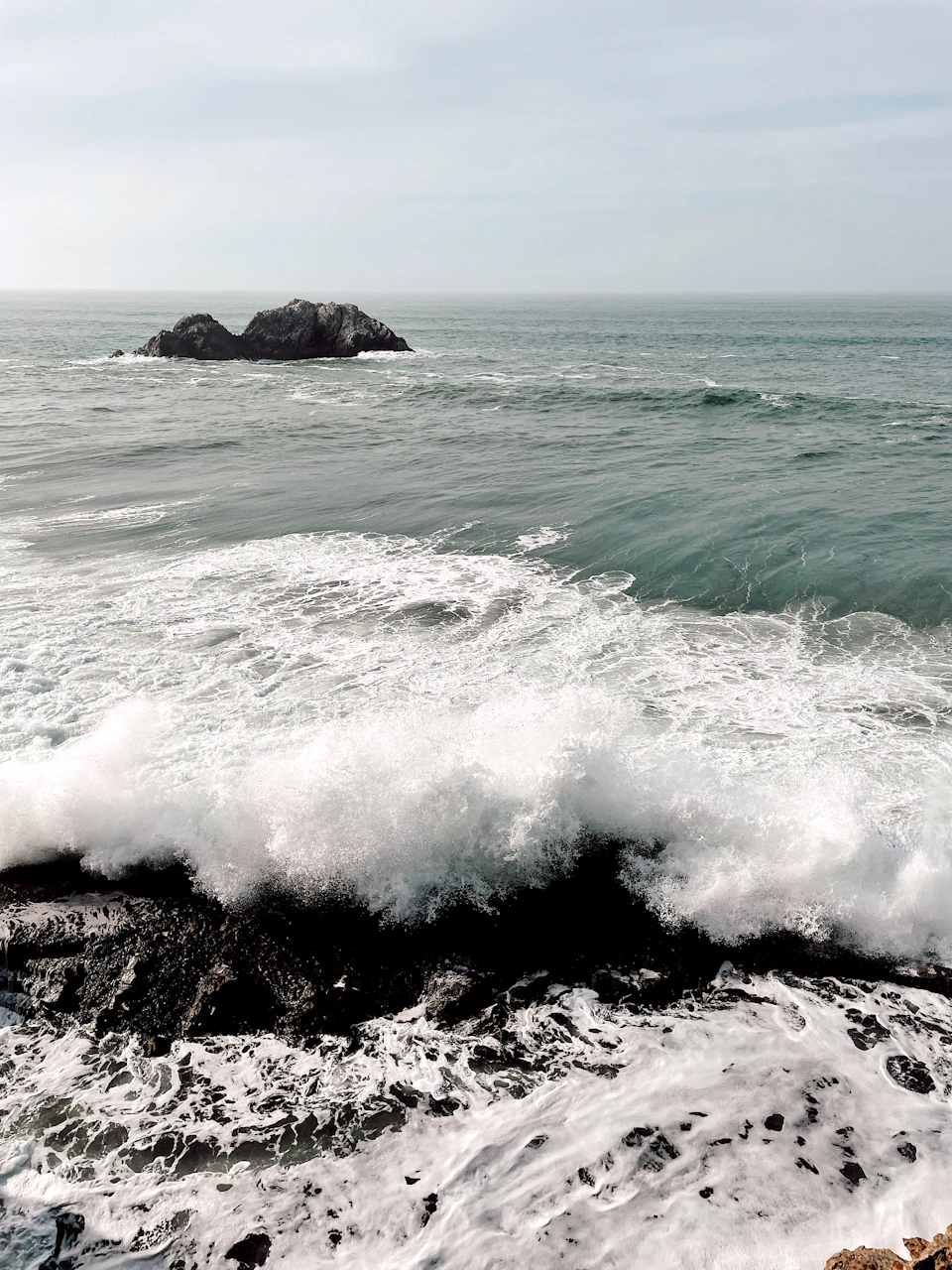 Two large rocks stand out from the rough, choppy ocean waters on a rocky coastline