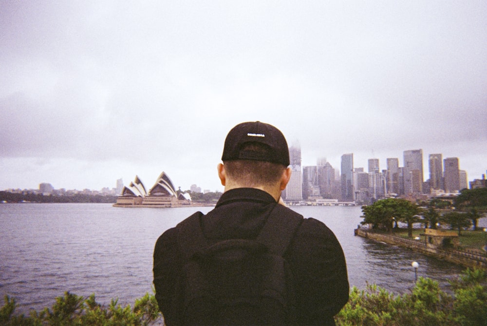 man in black jacket wearing black cap standing near body of water during daytime